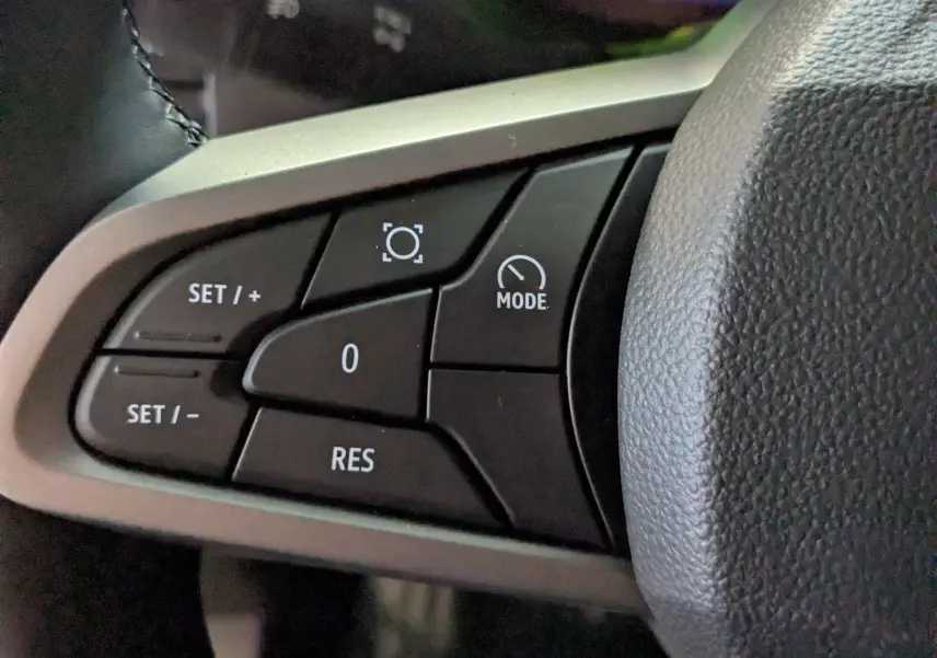 Gros plan sur les commandes du régulateur de vitesse au volant du Dacia Duster Hybrid 140 blanc glacier.