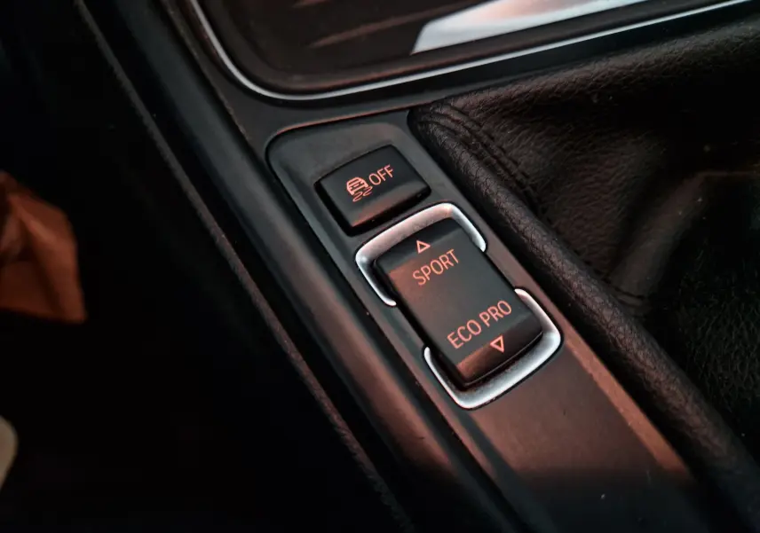 Gros plan sur les commandes de mode de conduite Sport et Eco Pro dans l'habitacle noir d'une BMW Série 3 316D 2014.