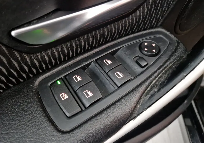 Gros plan sur les commandes électriques des vitres côté conducteur d'une BMW Série 3 316D noire de 2014.