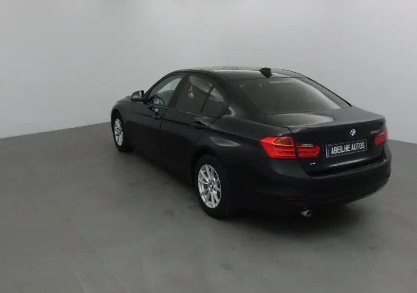 BMW Série 3 316d noire vue en 3/4 arrière droit, avec feux arrière rouges et jantes alliage argentées.