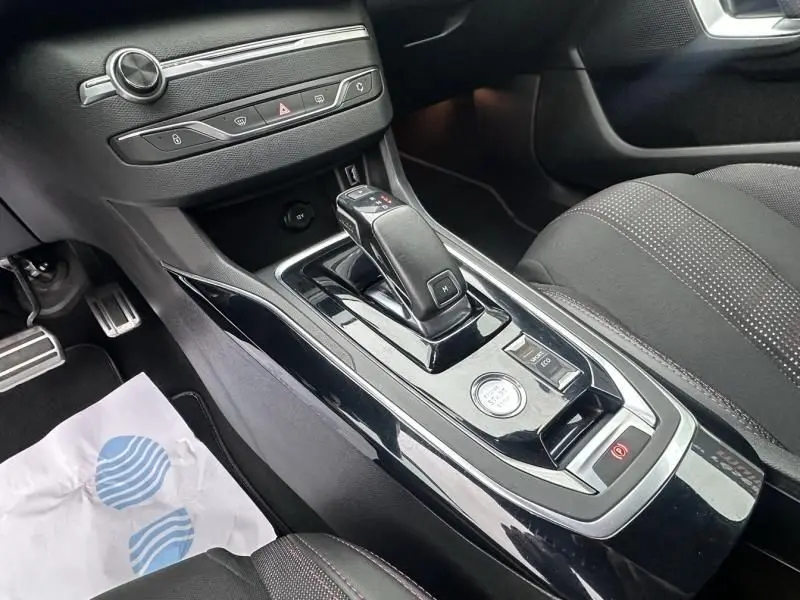 Vue rapprochée de la console centrale noire brillante de la Peugeot 308 gris métal, avec levier de boîte automatique et boutons de commande.