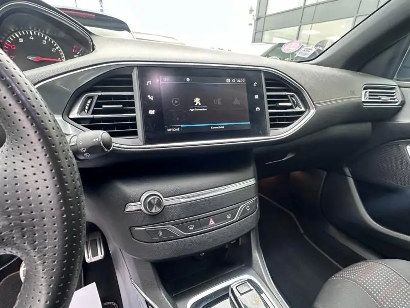 Vue intérieure côté conducteur du tableau de bord de la Peugeot 308 gris métal avec écran tactile et volant perforé.