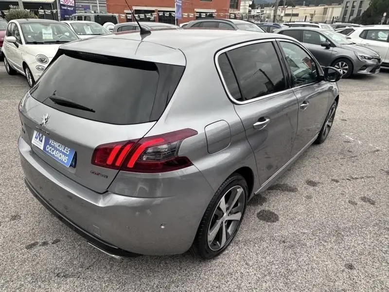 Peugeot 308 gris métal vue 3/4 arrière droit, feux arrière LED et vitres teintées, stationnée en extérieur.