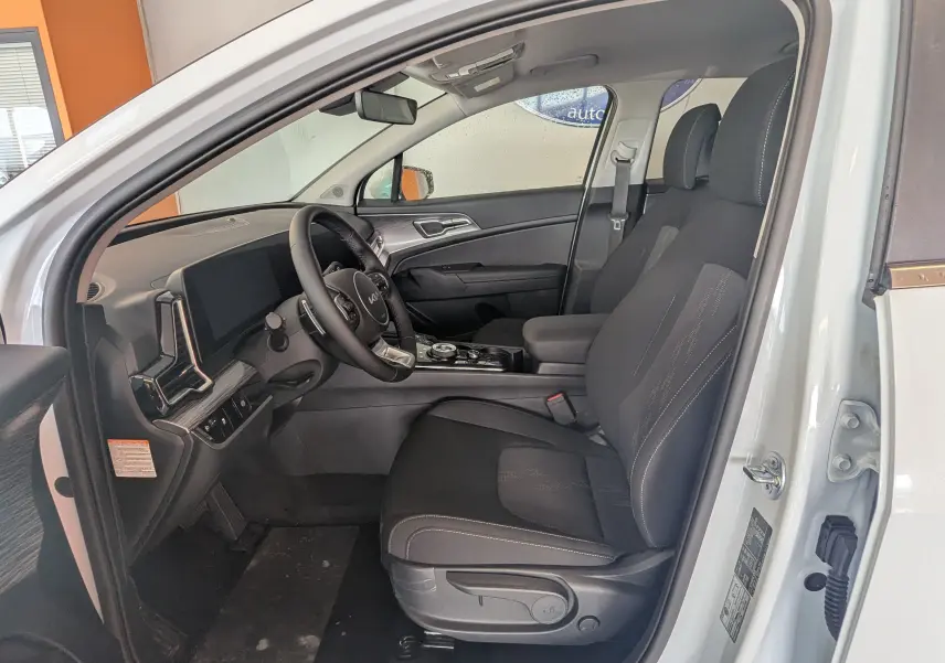 Vue intérieure côté conducteur du Kia Sportage blanc 2025, montrant les sièges noirs et le tableau de bord moderne.