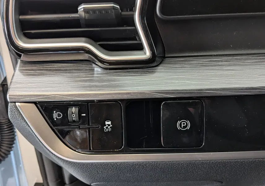 Détail du tableau de bord noir et gris avec commandes d'éclairage et frein à main électrique sur KIA SPORTAGE 2025.