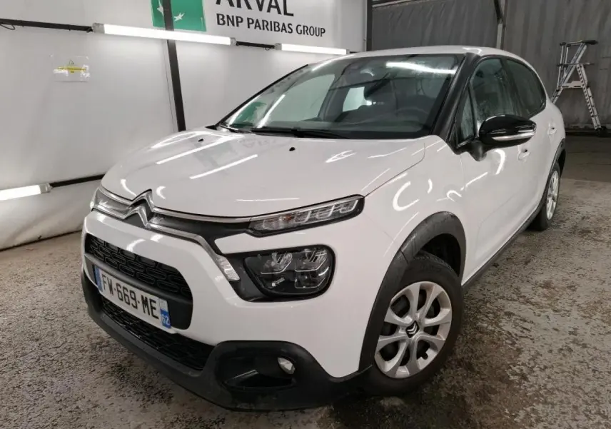Vue 3/4 avant droite d'une Citroën C3 blanche avec coques de rétroviseurs noires et jantes 15 pouces en intérieur industriel.