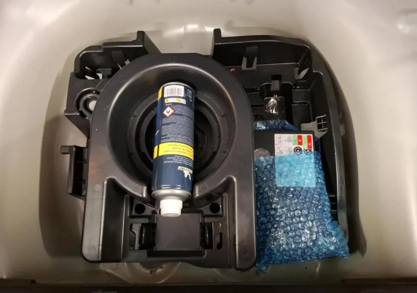 Vue rapprochée du coffre d'une Citroën C3 blanche montrant le kit de dépannage avec bombe anti-crevaison.