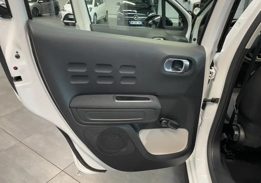 Vue intérieure sur la porte arrière gauche blanche d'une Citroën C3 2021 avec poignée et manivelle de vitre noire.
