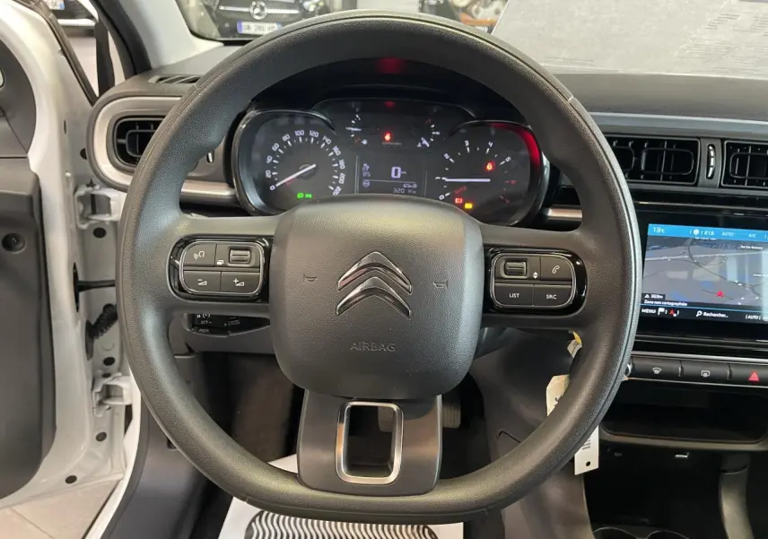 Vue intérieure centrée sur le volant noir de la Citroën C3 blanche avec tableau de bord et écran tactile visible à droite.