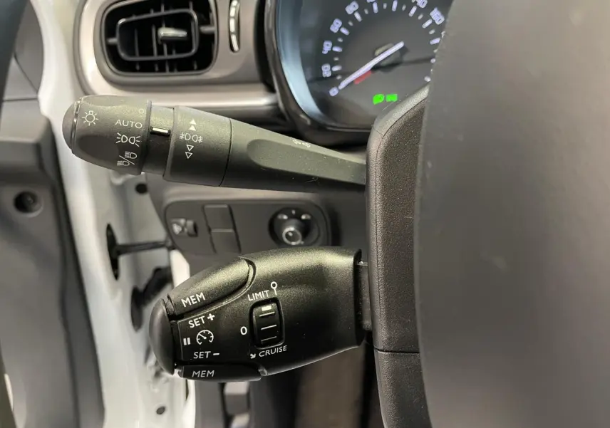 Gros plan sur les commandes au volant côté gauche de la Citroën C3 blanche, avec levier de clignotants et régulateur de vitesse.
