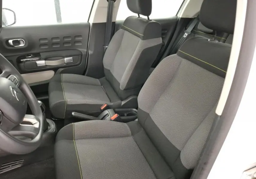 Vue intérieure côté gauche de la Citroën C3 blanche, montrant les sièges avant gris à surpiqûres jaunes et la portière.