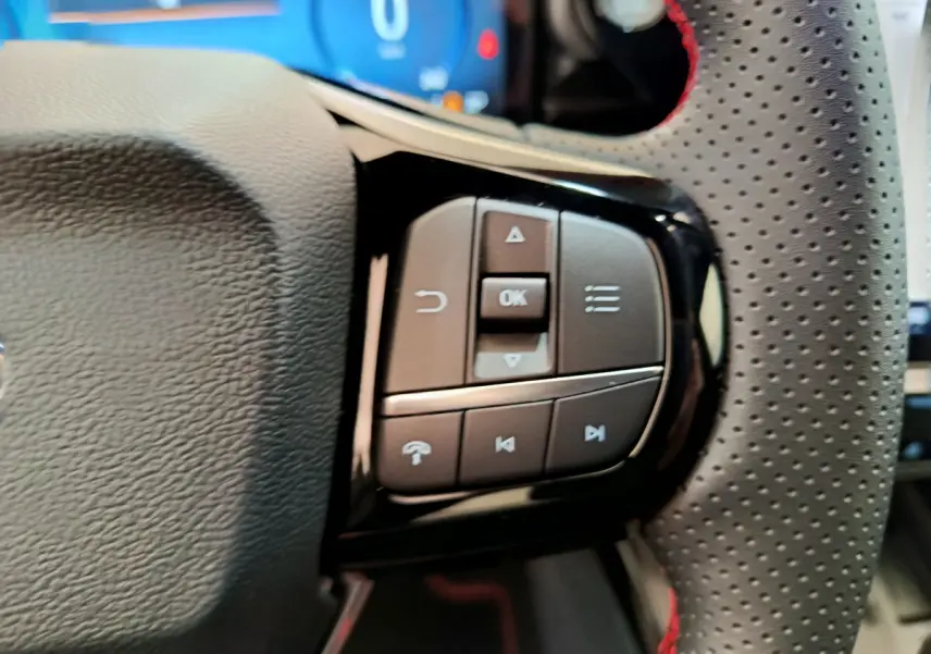 Gros plan sur les commandes multifonctions noires à droite du volant perforé avec surpiqûres rouges du Ford Puma bleu.