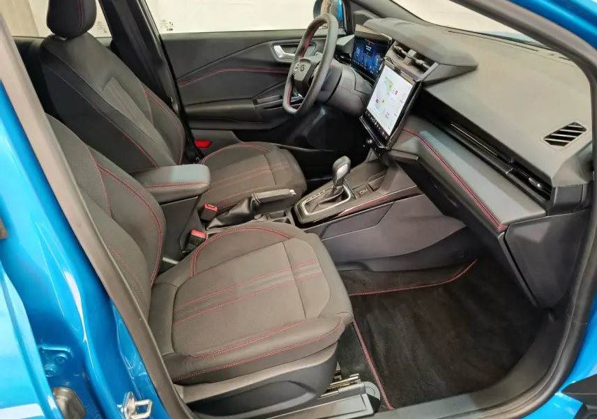 Vue intérieure côté conducteur du Ford Puma bleu 2025, sièges noirs avec surpiqûres rouges et écran tactile central.