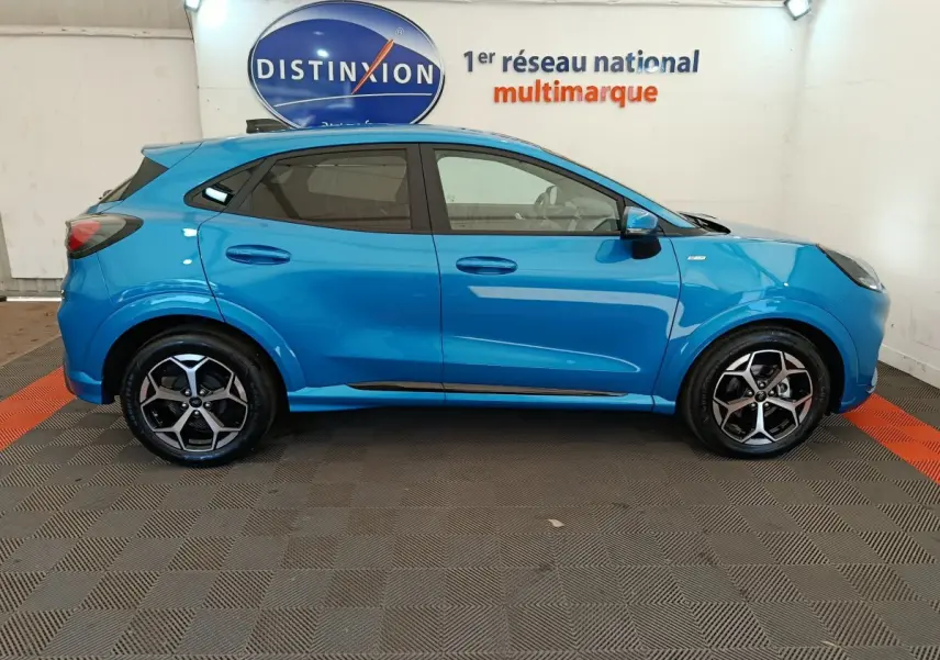 Vue de profil côté gauche d'un Ford Puma bleu 2025 ST-LINE avec jantes alliage et vitres teintées, en intérieur showroom.