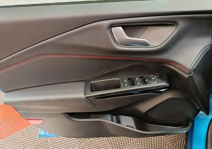 Vue intérieure côté gauche de la porte d’une Ford Puma bleue avec surpiqûres rouges et commandes électriques.