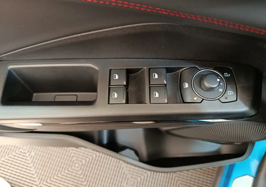 Vue rapprochée des commandes de lève-vitres et rétroviseurs sur la porte côté conducteur d’un Ford Puma bleu.