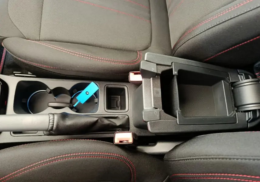 Vue plongeante sur la console centrale noire avec accoudoir ouvert et sièges noirs à surpiqûres rouges du Ford Puma bleu.
