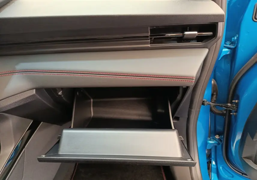 Vue intérieure côté passager du Ford Puma bleu 2025, boîte à gants ouverte avec surpiqûres rouges sur le tableau de bord.