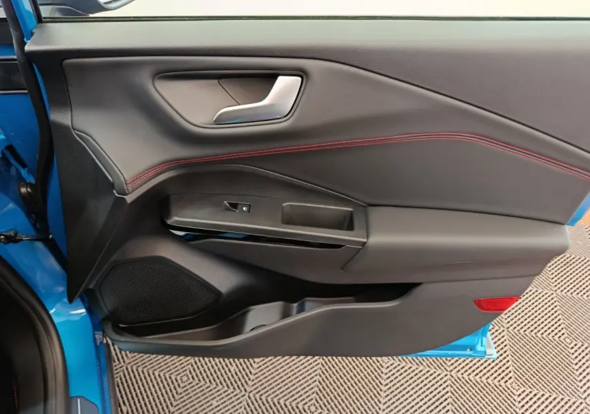 Vue rapprochée de la porte avant gauche bleu vif du Ford Puma 2025, avec surpiqûres rouges et poignée argentée.