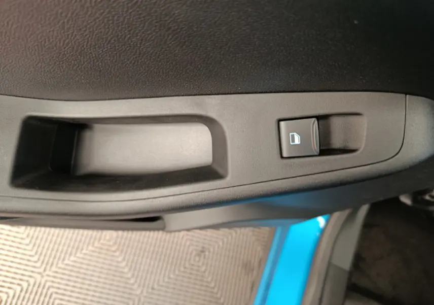 Gros plan sur la poignée intérieure de porte côté droit du Ford Puma bleu, avec bouton de verrouillage des vitres.