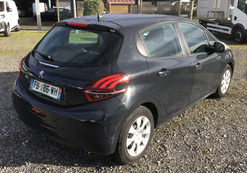 Vue 3/4 arrière droite d'une Peugeot 208 noire 2018 avec feux arrière distinctifs et jantes blanches sur sol gravillonné.