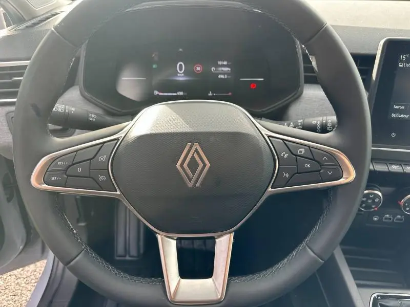 Vue rapprochée du volant noir de la Renault Clio 2025 avec commandes intégrées et tableau de bord numérique en arrière-plan.