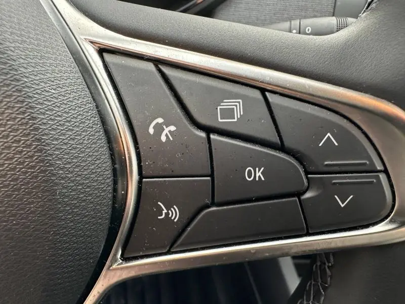 Gros plan sur les commandes multifonctions noires du volant côté gauche de la Renault Clio 2025, entourées de chrome.