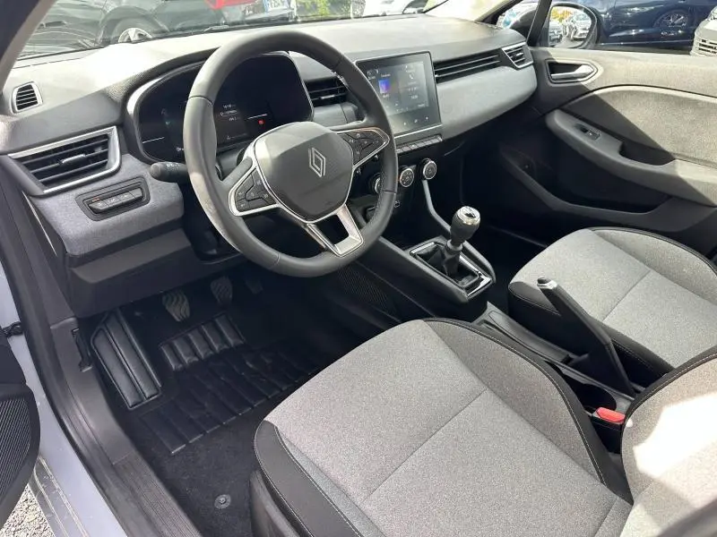 Vue intérieure côté conducteur de la Renault Clio 2025, montrant le volant, la boîte manuelle et les sièges gris clair.