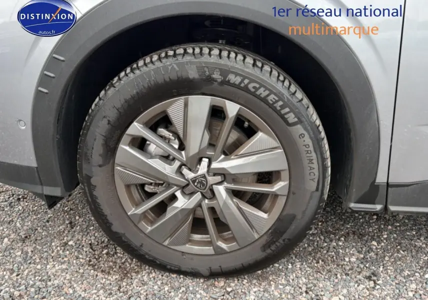 Gros plan sur la roue avant gauche avec jante alu et logo Peugeot du SUV 5008 gris Artense.