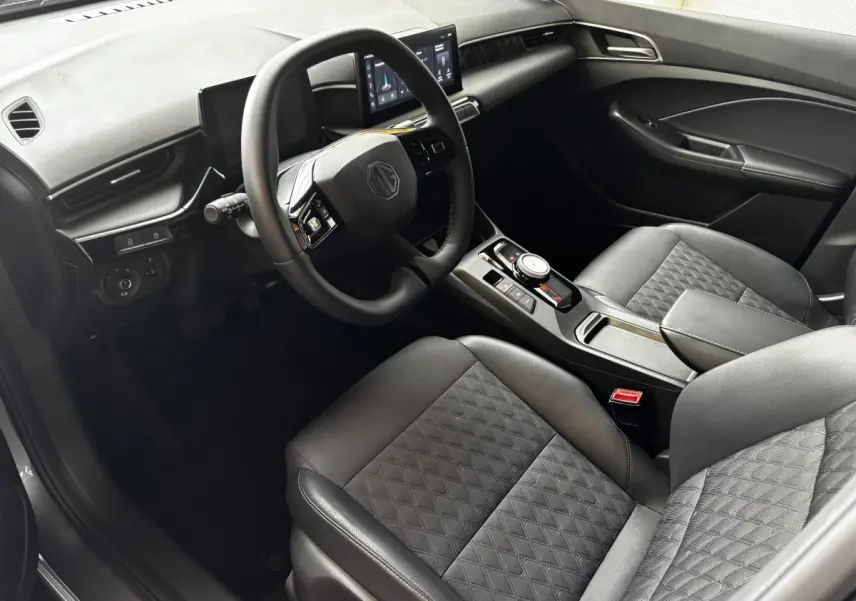 Intérieur de MG3 1.5L Hybrid+ Luxury 2025 vu côté conducteur, volant suede multifonctions et sièges gris matelassés.