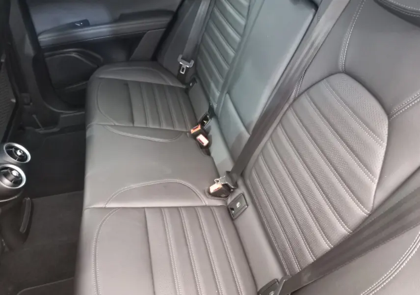 Vue intérieure sur la banquette arrière en cuir gris foncé de l'Alfa Romeo Stelvio 2024 avec ceintures et aérateurs.