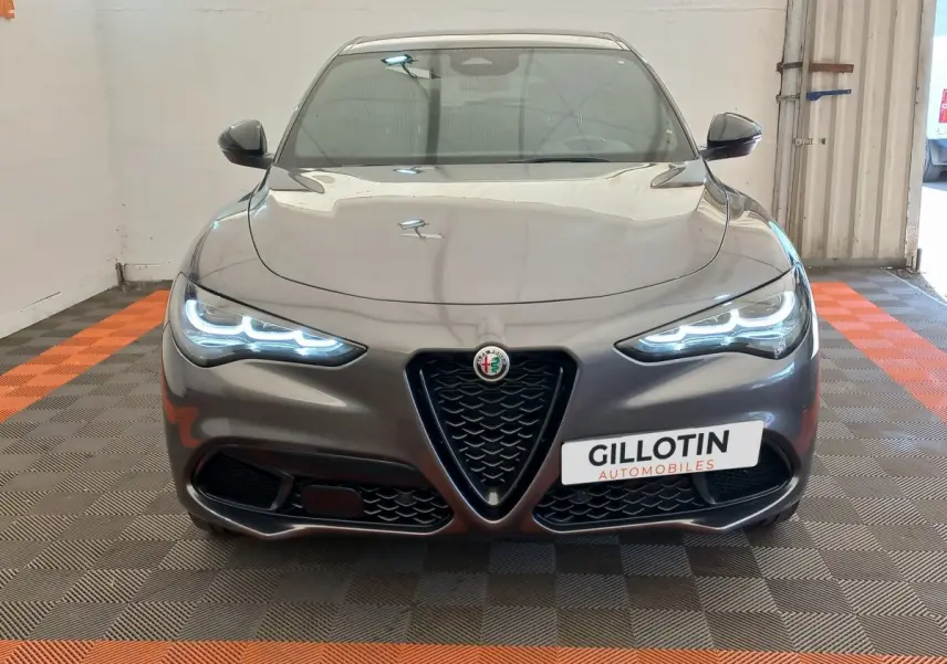 Vue frontale d'une Alfa Romeo Stelvio gris foncé 2024 avec phares LED allumés et calandre caractéristique en V.