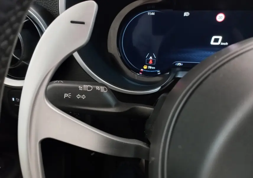 Gros plan sur le combiné d'instruments numérique et la palette de changement de vitesse alu du volant de l'Alfa Romeo Stelvio gris foncé.