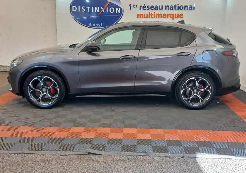 Vue de profil côté gauche d'un Alfa Romeo Stelvio gris foncé avec jantes sport et étriers rouges.