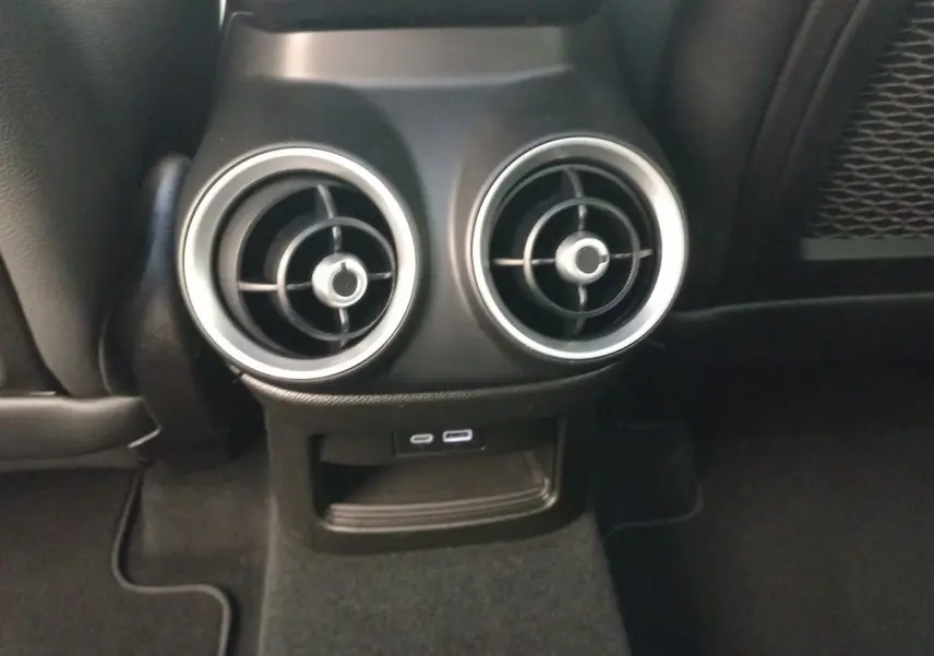 Détail des aérateurs arrière ronds avec bordure alu et prises USB dans l’habitacle noir de l’Alfa Romeo Stelvio 2024.