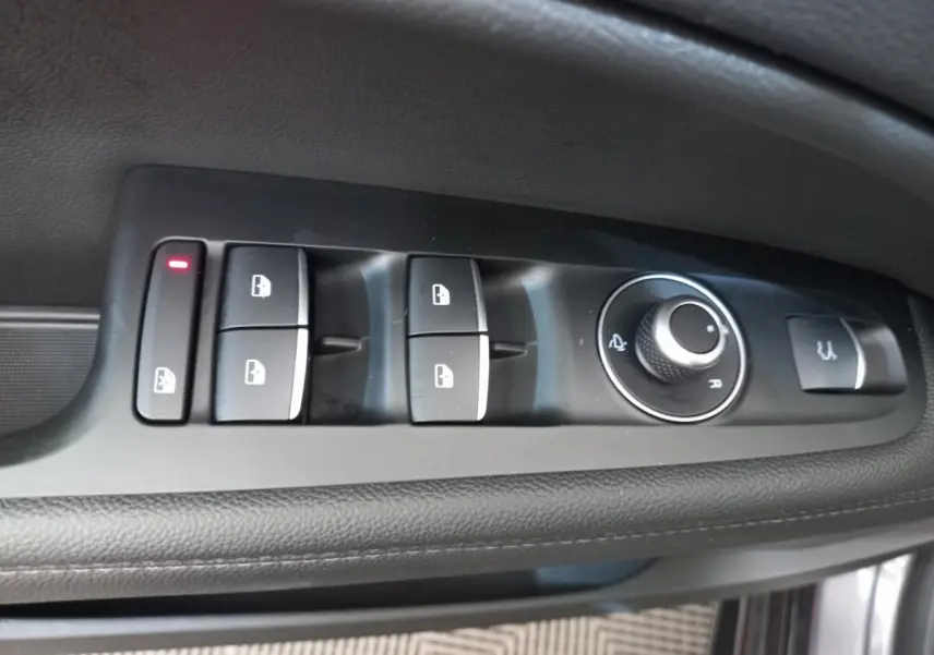Gros plan sur les commandes de lève-vitres et rétroviseurs côté conducteur de l'Alfa Romeo Stelvio gris foncé.
