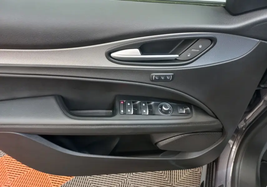 Gros plan sur la porte avant gauche gris foncé de l'Alfa Romeo Stelvio 2024 avec commandes électriques et poignée argentée.