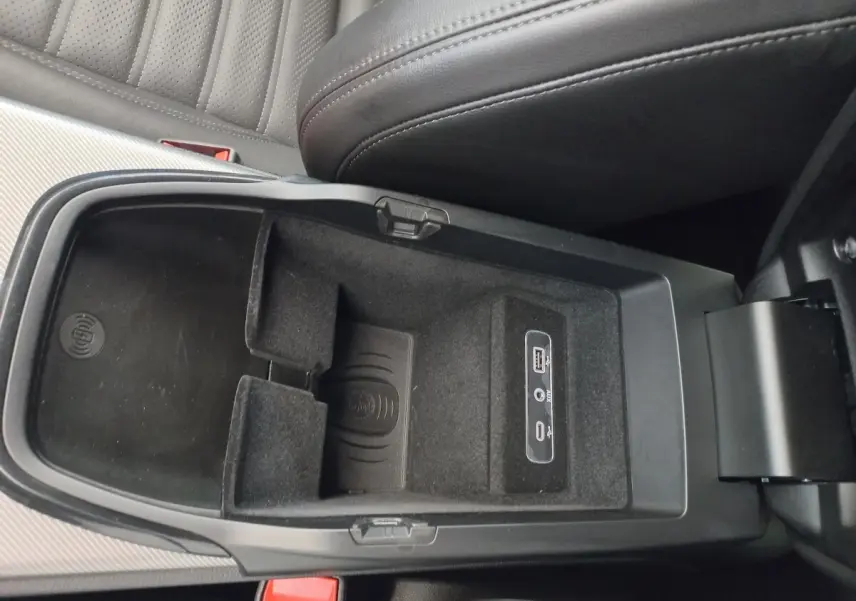 Vue intérieure du compartiment central ouvert de l'Alfa Romeo Stelvio gris foncé, montrant la zone de recharge par induction et ports USB.