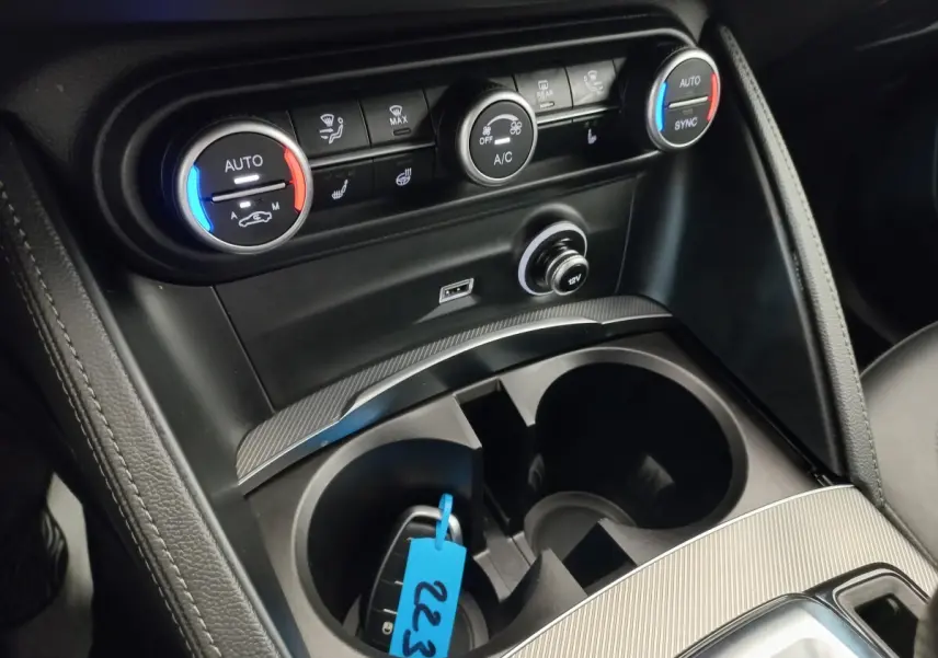 Gros plan sur la console centrale de l'Alfa Romeo Stelvio 2024, avec commandes climatisation et prise 12V visibles.