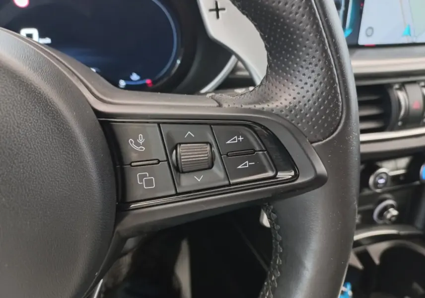 Gros plan sur les commandes du volant cuir perforé de l'Alfa Romeo Stelvio gris foncé, avec tableau de bord en arrière-plan.