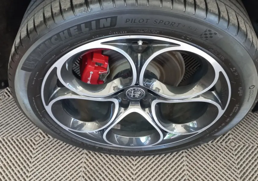 Gros plan sur la jante alu noire et argentée avec logo Alfa Romeo et étrier de frein rouge du Stelvio gris foncé.