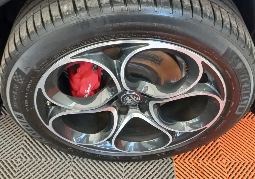 Gros plan sur la roue avant avec jante noire et argentée, étrier de frein rouge Alfa Romeo visible.