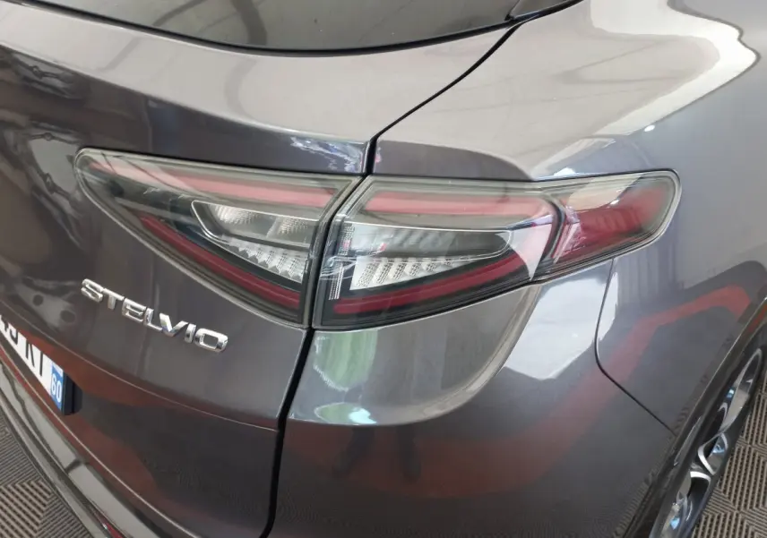 Gros plan sur le feu arrière droit et le logo Stelvio d’un Alfa Romeo gris foncé, vue arrière en légère plongée.