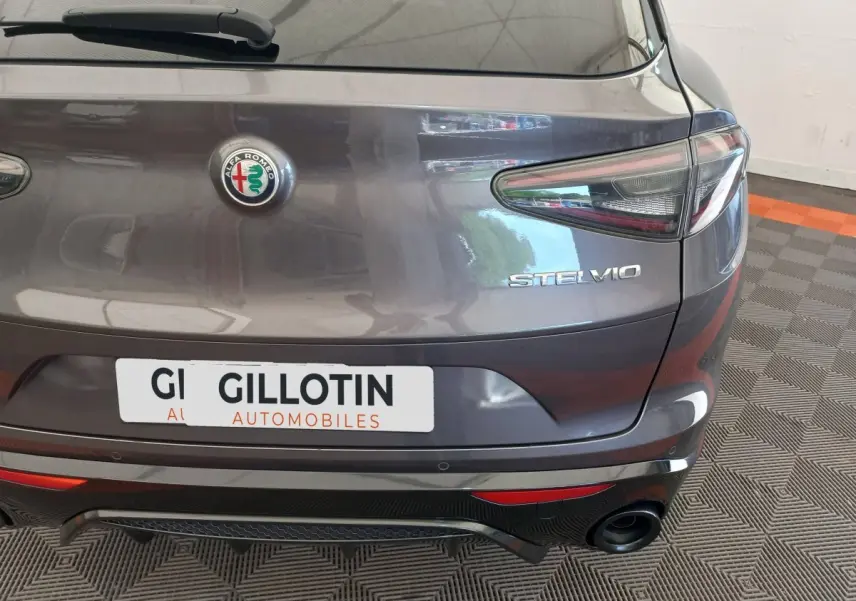 Vue arrière d'un Alfa Romeo Stelvio gris foncé avec logo central et feux arrière allongés, en intérieur showroom.