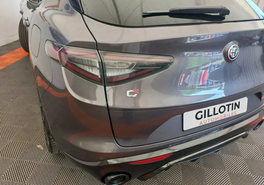 Vue 3/4 arrière droite de l'Alfa Romeo Stelvio gris foncé avec feux LED et double sortie d'échappement visible.