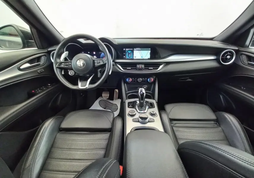 Vue intérieure avant de l'Alfa Romeo Stelvio gris foncé, avec tableau de bord moderne et écran tactile central.