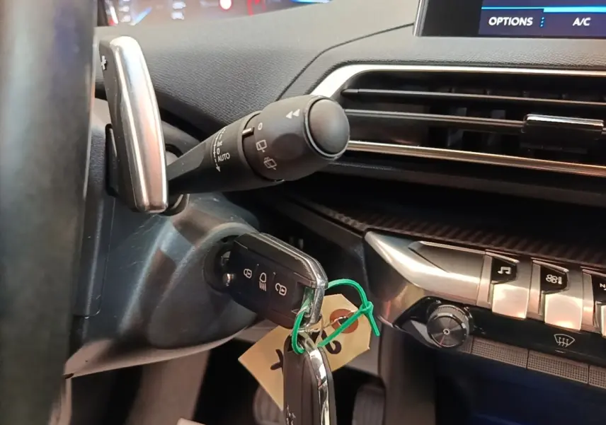 Gros plan sur le volant cuir et la clé insérée dans le contacteur d'une Peugeot 3008 noire, tableau de bord et commandes visibles.