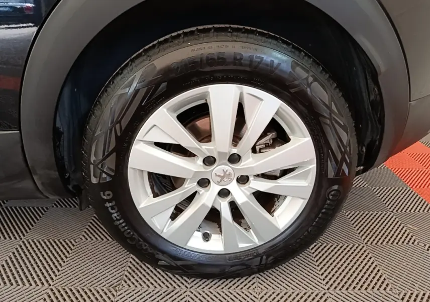 Gros plan sur la roue avant droite du Peugeot 3008 noir, mettant en valeur la jante alliage et le logo lion central.