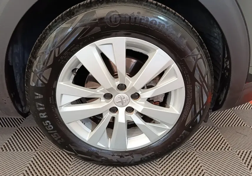Gros plan sur la roue avant droite avec jante argentée du Peugeot 3008 noir, montrant le logo lion central.