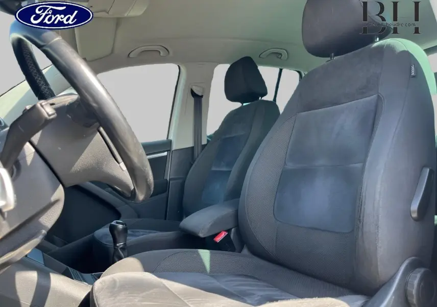 Vue intérieure côté conducteur montrant les sièges sport en tissu noir et alcantara avec accoudoir central.